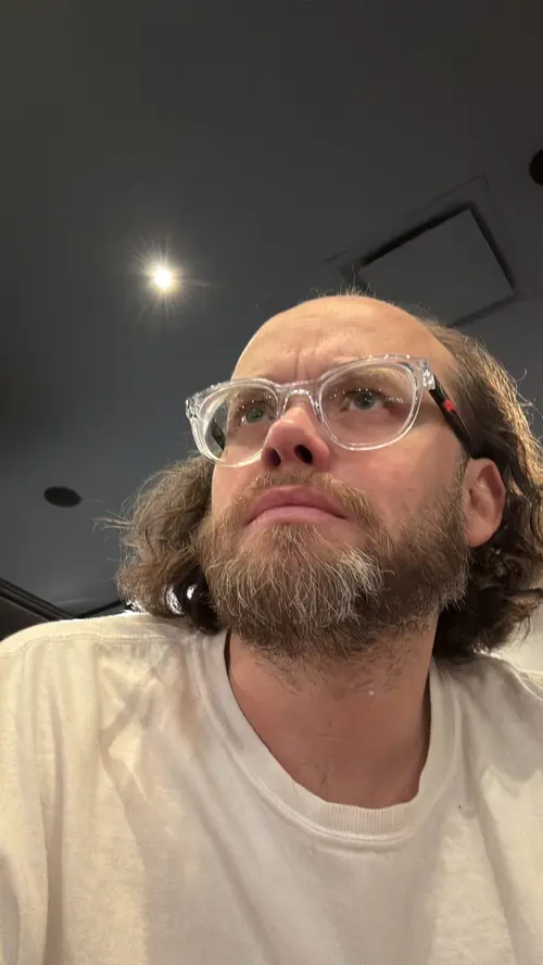 Esteban Rey posa serio en una habitación oscura con gafas transparentes.